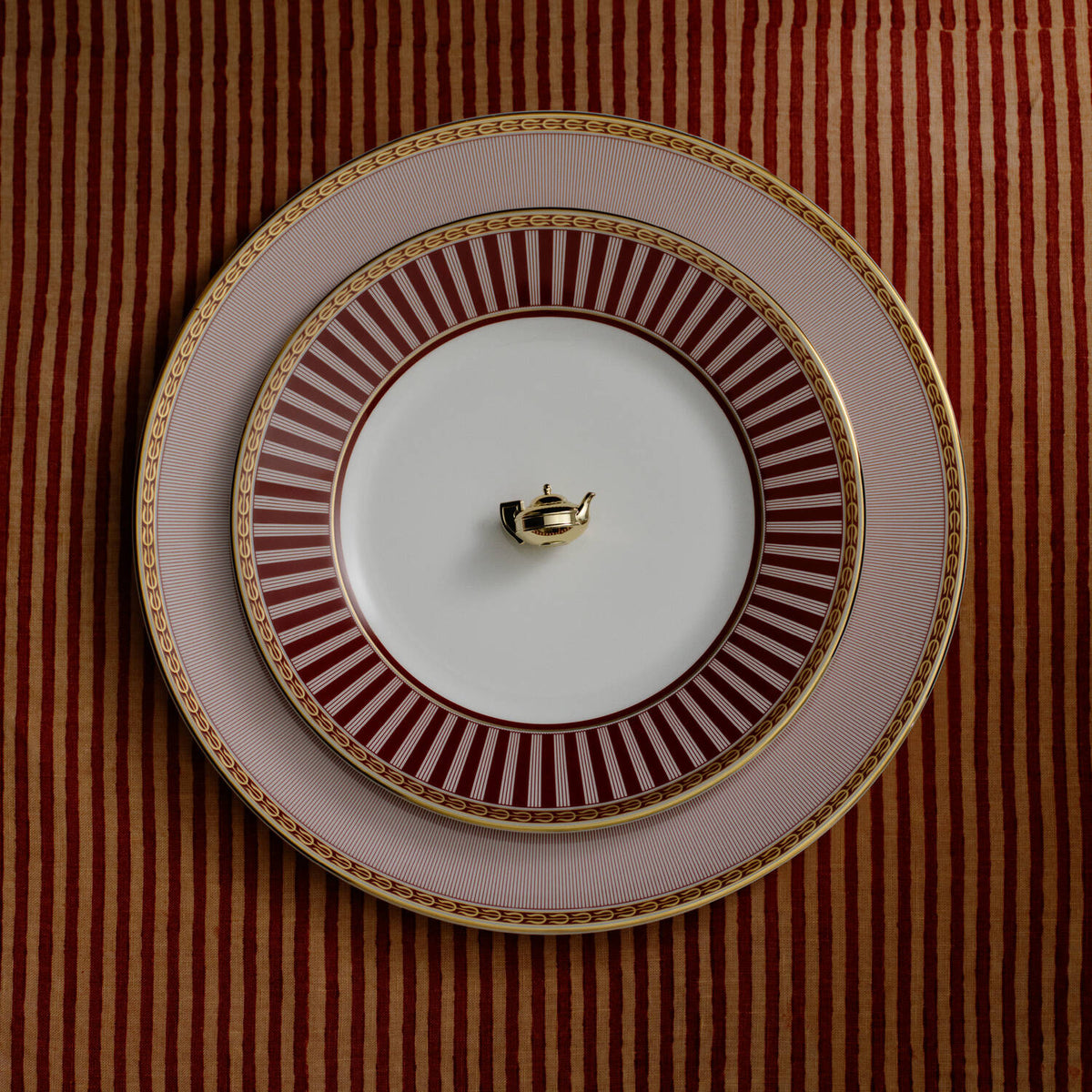 Splendour Red Side Plate - A set of three stacked Red Splendour ceramic plates, all set against a matching red and gold striped tablecloth.