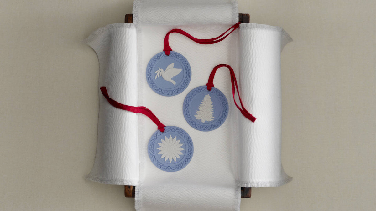 Three Jasperware round blue and white hanging ornaments with red ribbons, displayed on a white paper scroll against a light beige background.