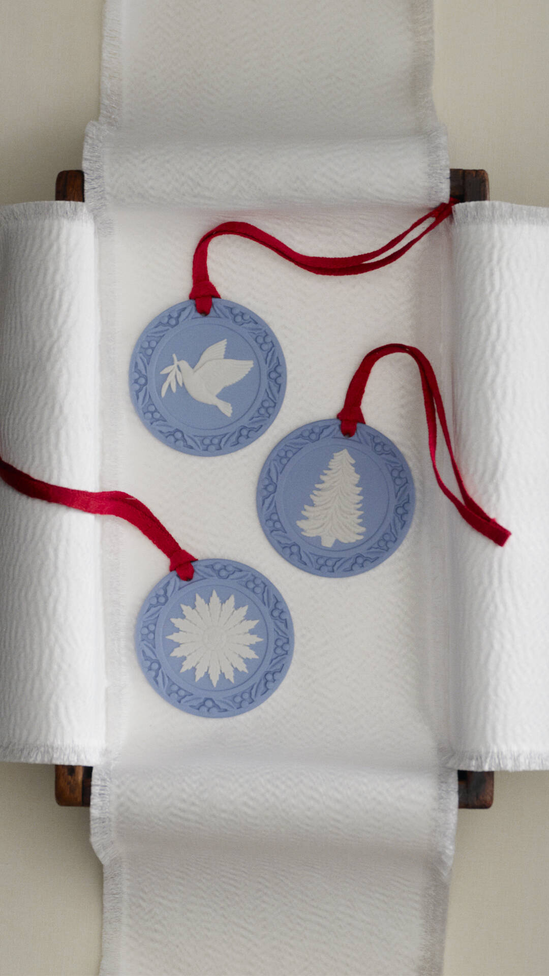 Three Jasperware round blue and white decorative hanging ornaments with red strings, displayed on a white textured fabric backdrop.
