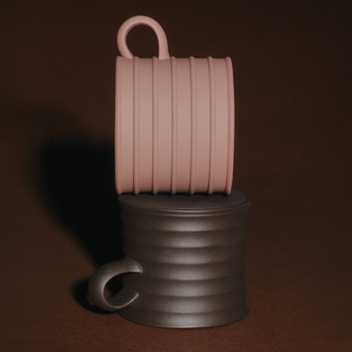 JW Anderson Mug Pair Dark Brown / Teracotta - Two ribbed JW Anderson jasperware mugs stacked vertically on a dark brown background. The top mug is a dusty pink color, and the bottom mug is a dark brown.