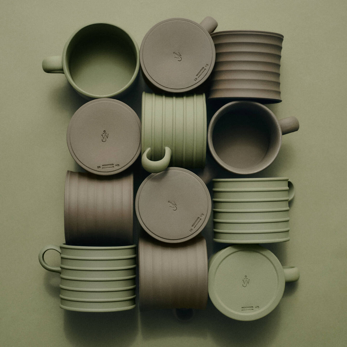 JW Anderson Mug Pair Marsh Green / Sage Green - A collection of JW Anderson jasperware mugs and matching lids arranged in a grid on a solid sage green background. The set features two primary colors: a muted sage green and a taupe-brown.