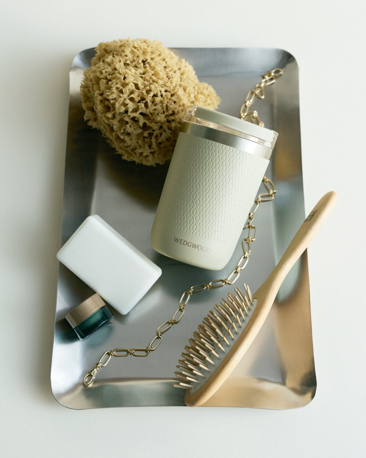 Set of beauty tools including a brush, sponge, and a Gio travel mug in sage green on a reflective surface.