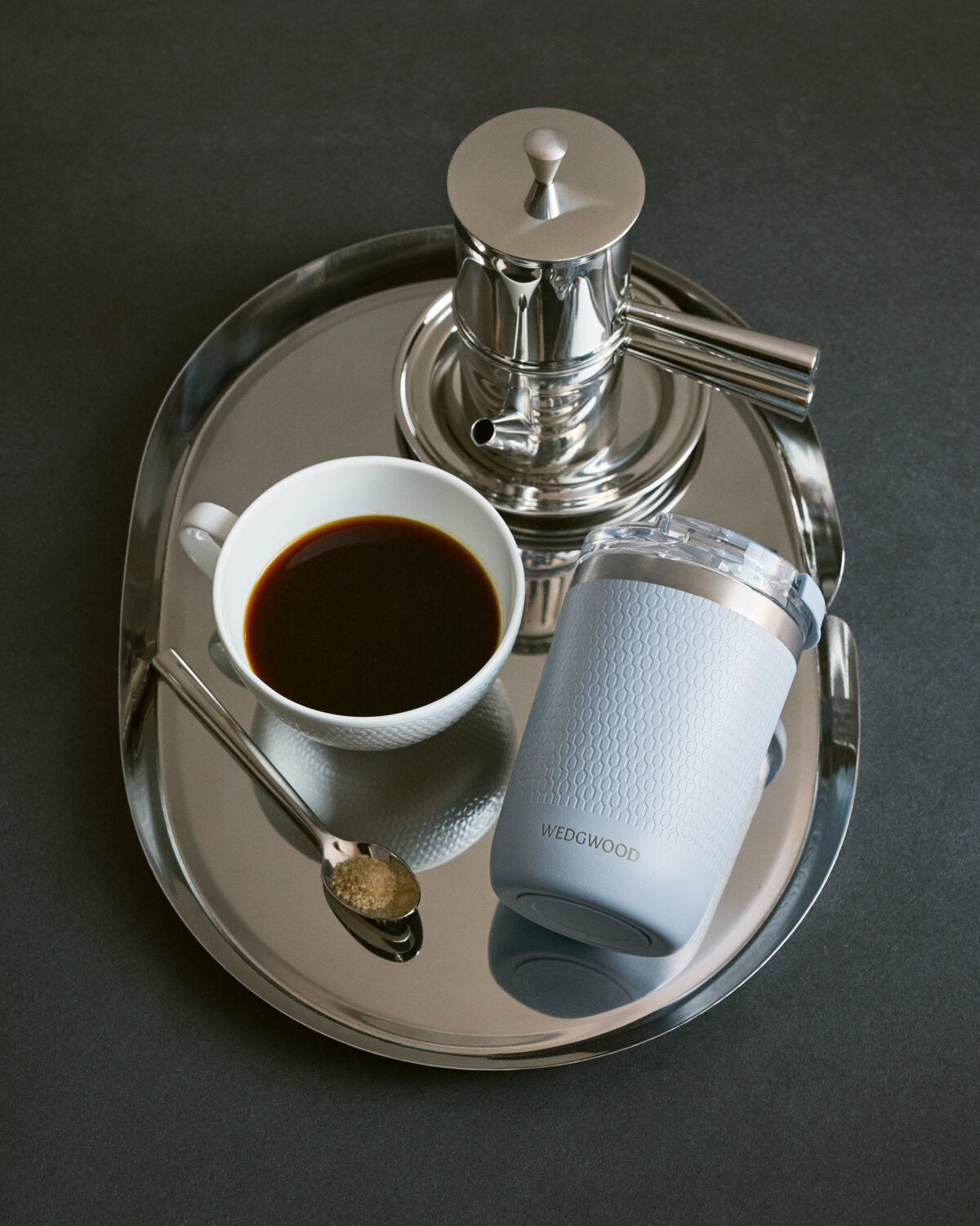 Silver platter with a cup of coffee, spoon, and Wedgwood blue travel mug on a dark background